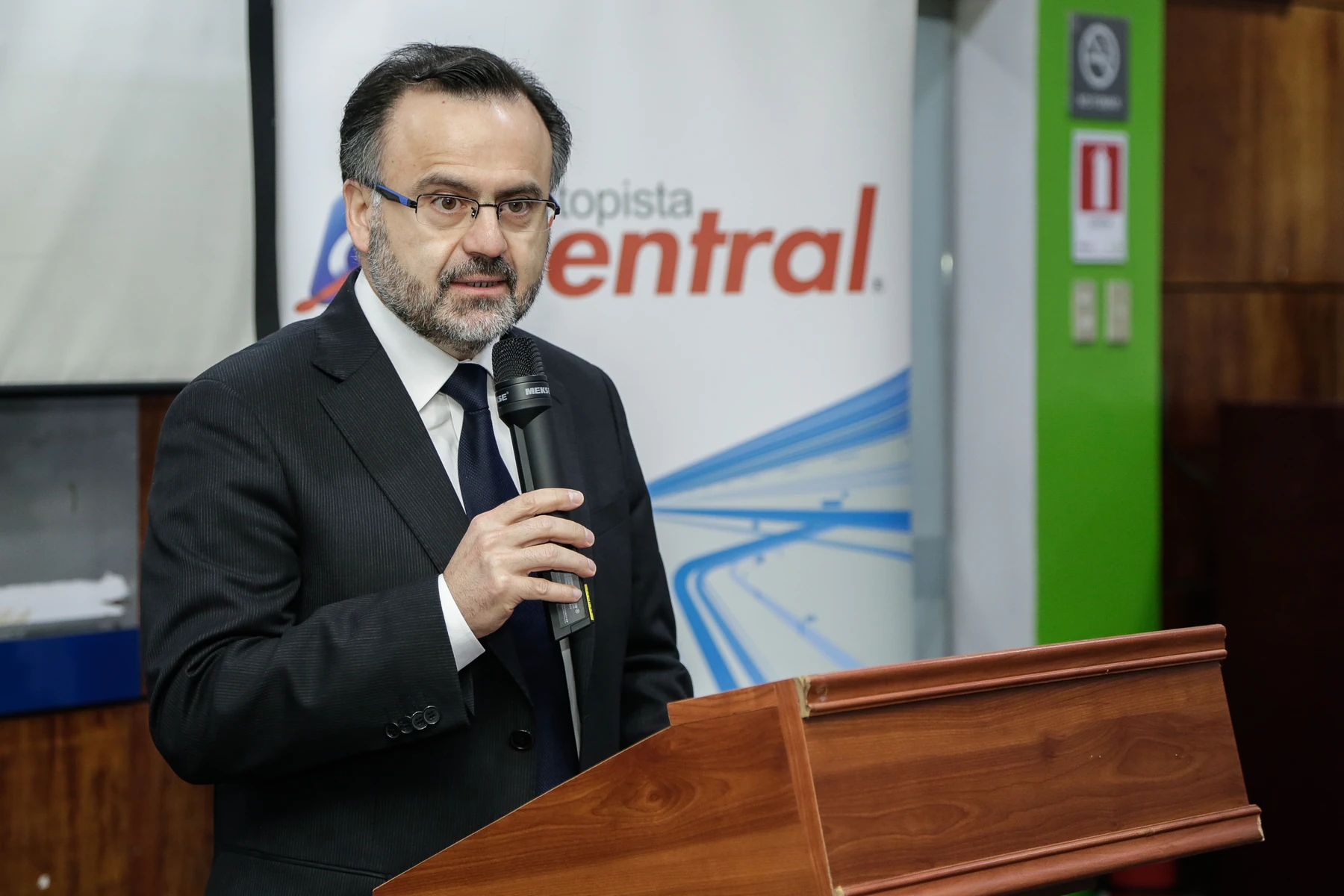 Exposición con micrófono junto a un atril de madera y un letrero de Autopista Central
