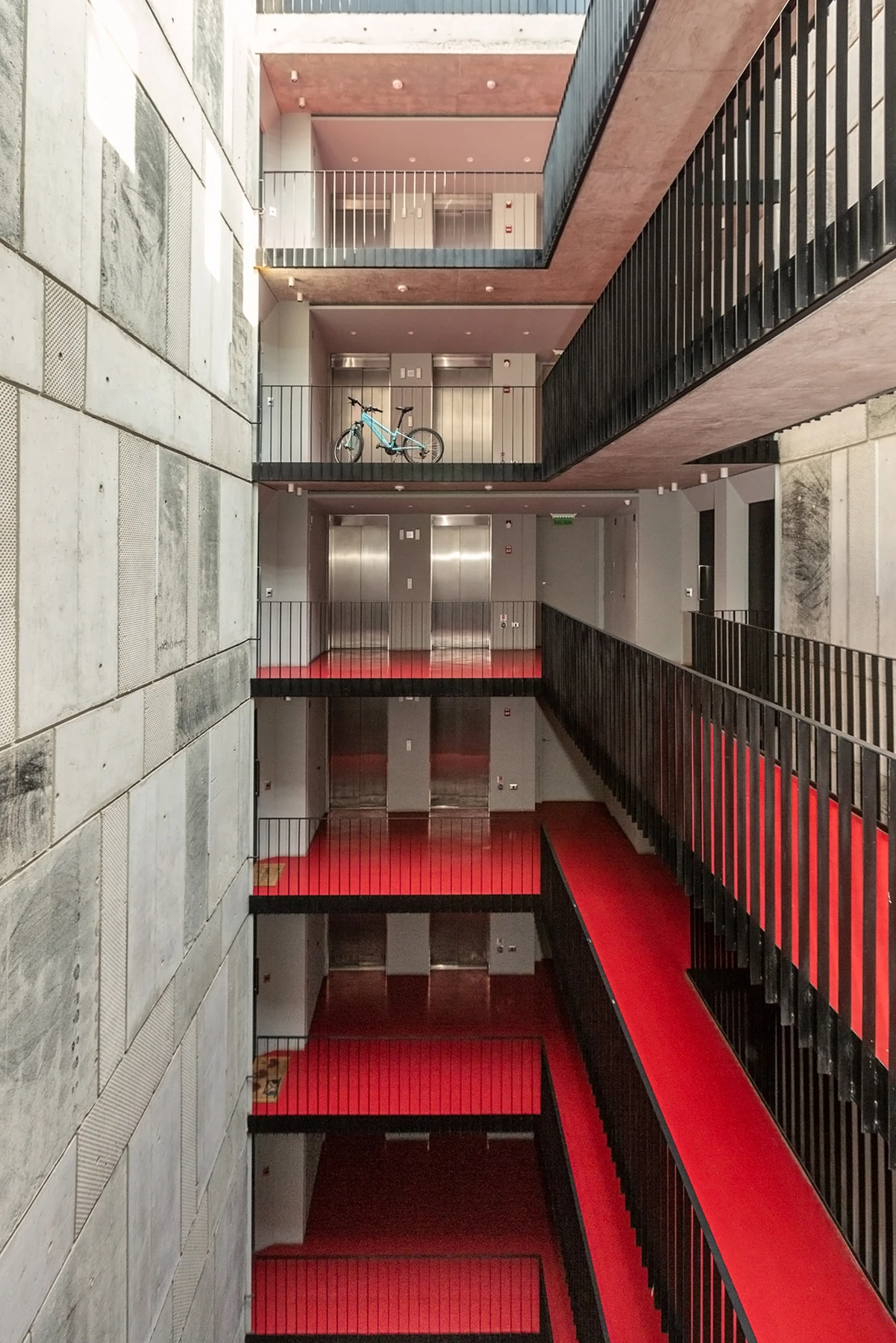 Patio interior de un edificio con pasillos rojos, barandas negras y ascensores